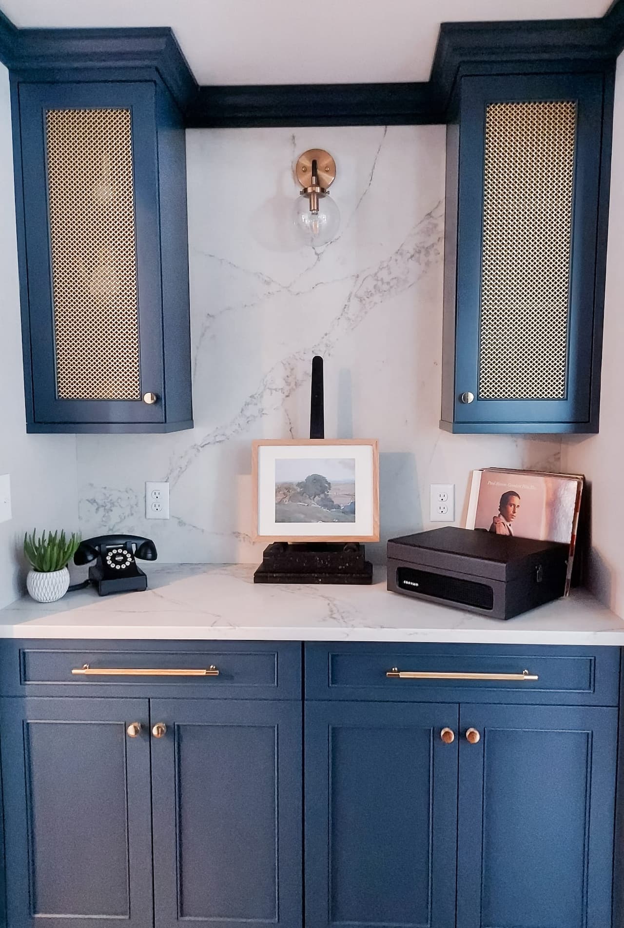 Butler's pantry in navy cabinetry with brass hardware, caned upper doors and a marble slab backsplash