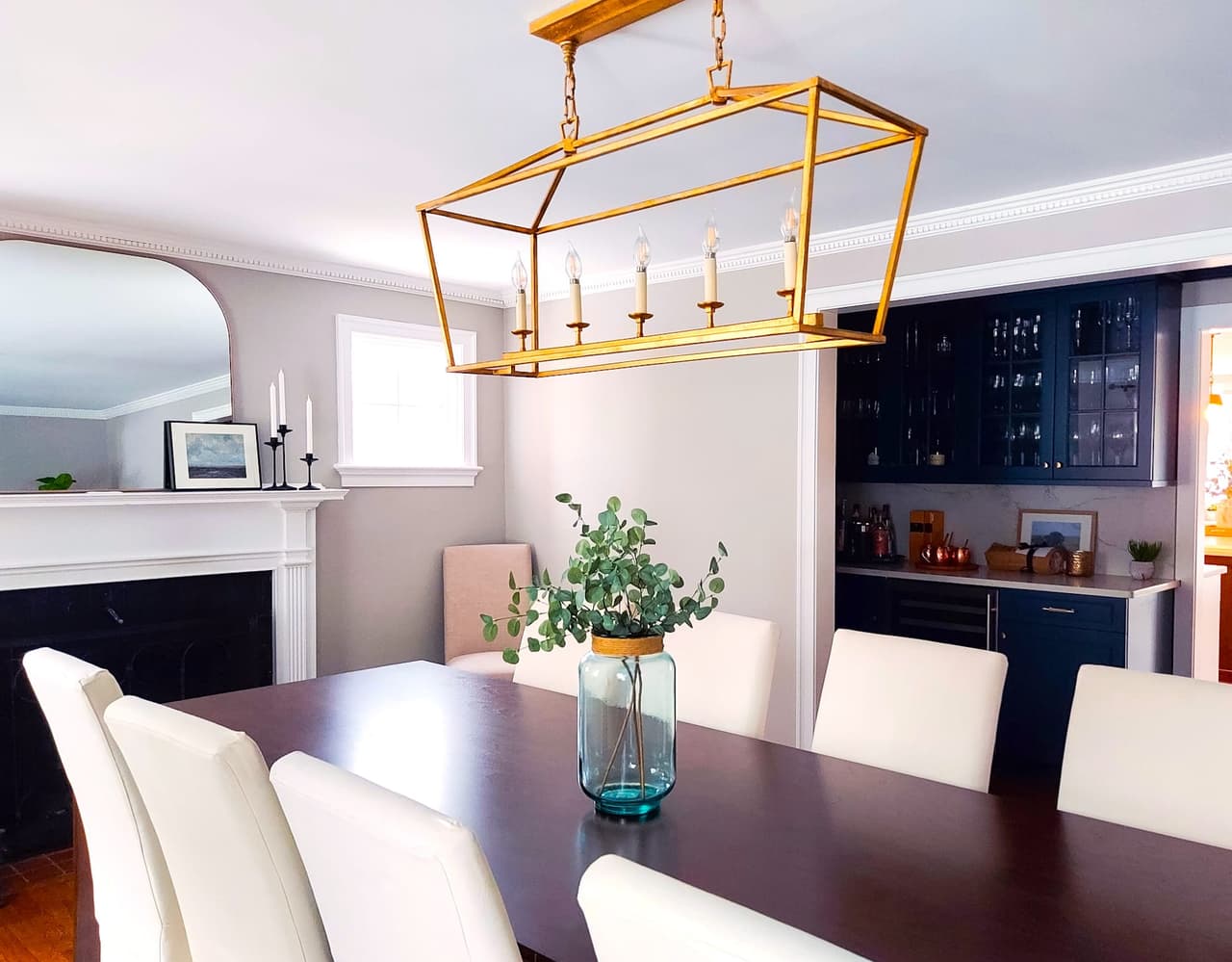 Dining room with a dark table, white upholstered chairs and a brass lantern chandelier, with the navy butler's pantry beyond