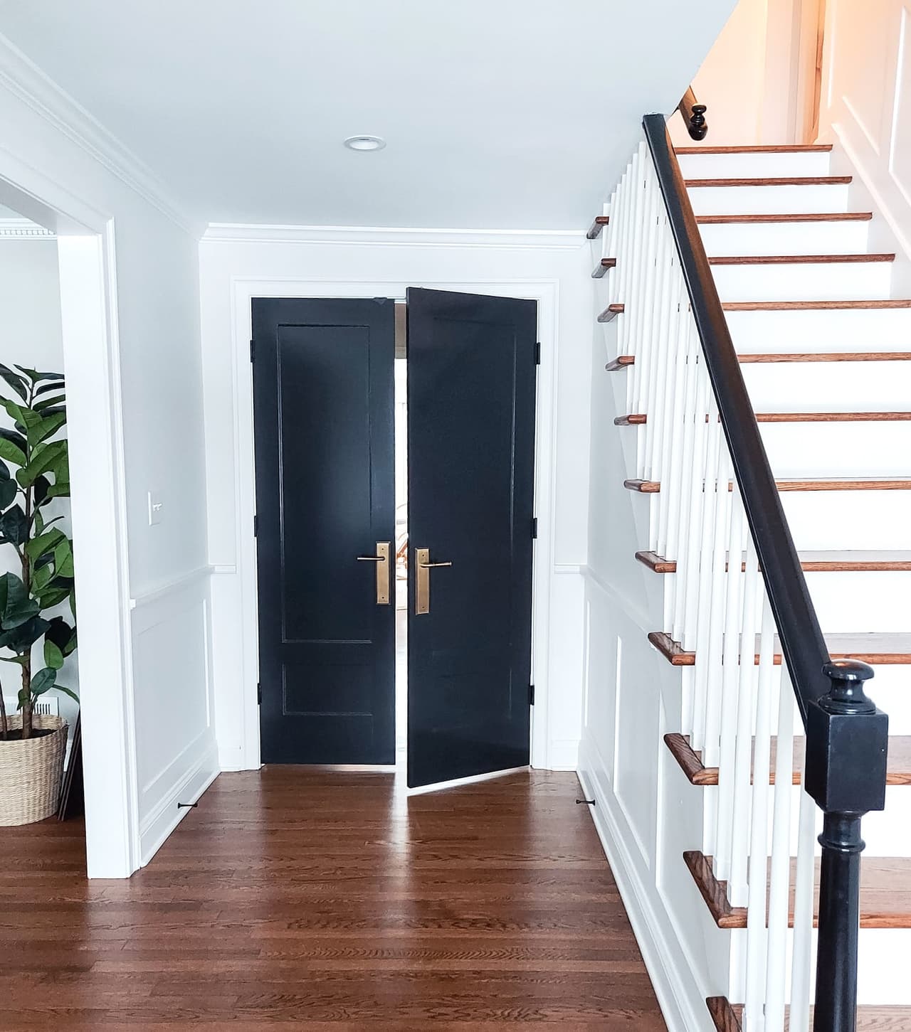 Entry hall with navy double doors, brass hardware, a white-balustered stair and dark stained floors