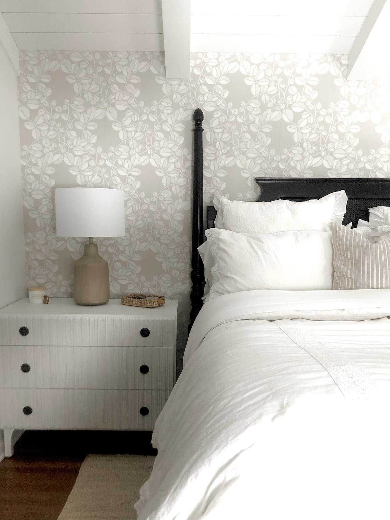 Primary bedroom with a dark four-poster bed against a patterned wallcovering, between woven nightstands