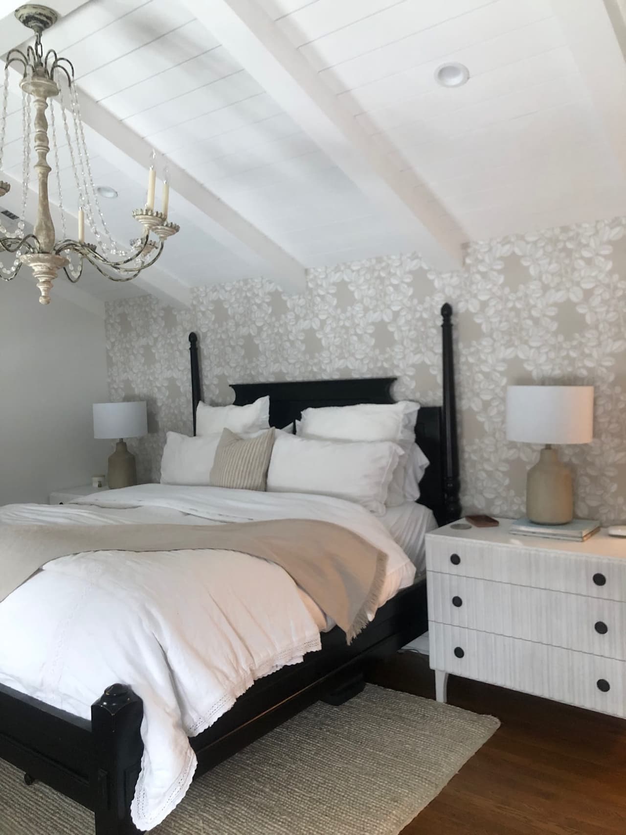 Primary bedroom under a sloped ceiling with a crystal chandelier, a dark four-poster bed and paired nightstands