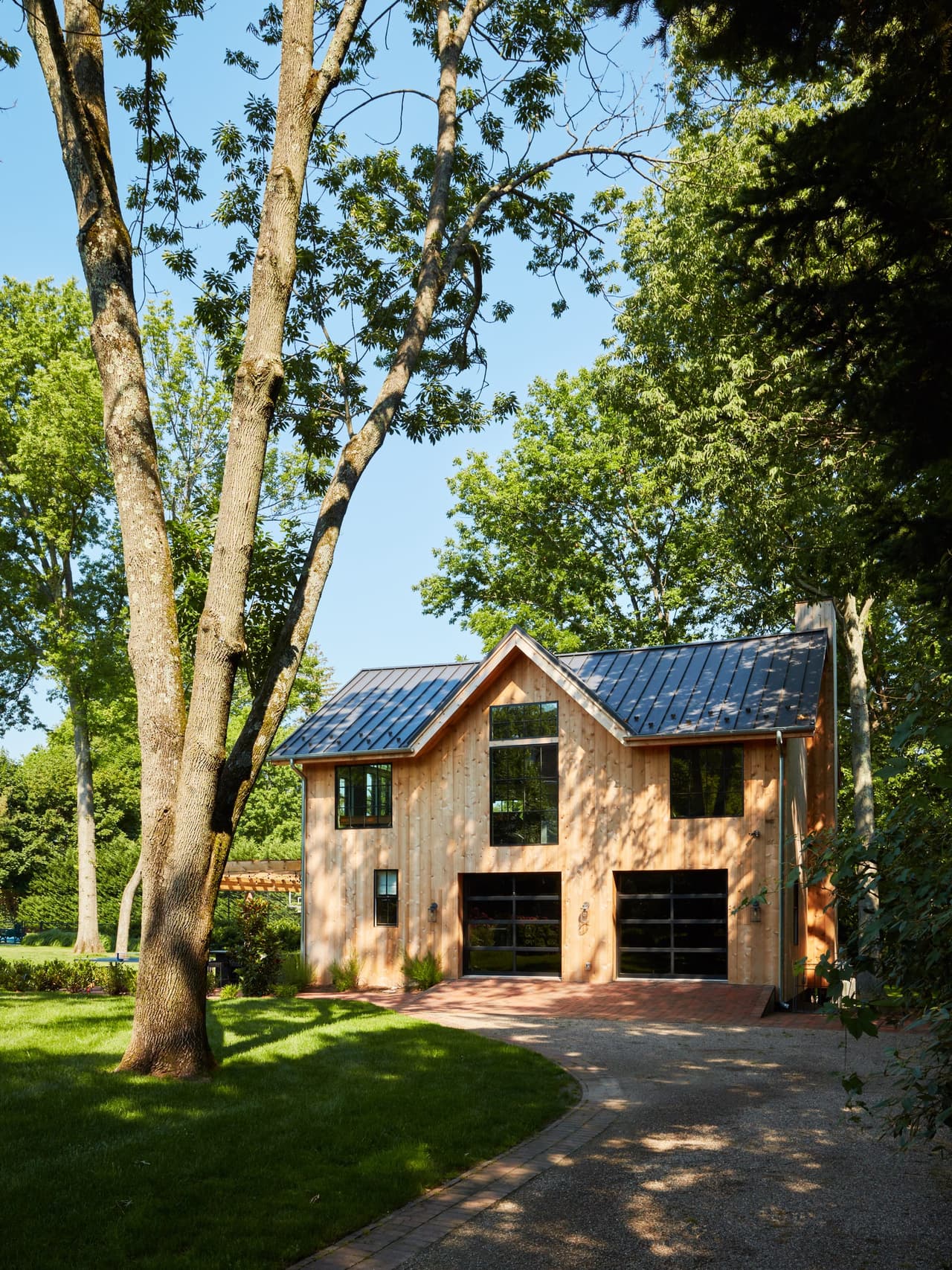 The renovated backyard barn seen across the lawn under mature trees, in Westfield, NJ