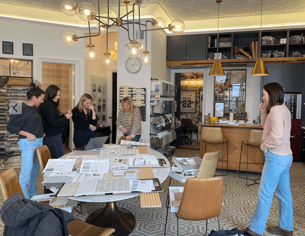 The Ellie Mroz Design studio with the team reviewing fabric, tile and paint selections spread across a round table