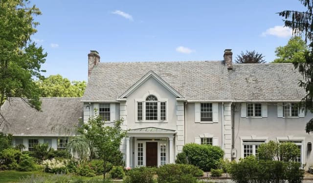 The front of a Mendham, NJ house before its whole-home renovation, a stucco colonial with a pedimented center gable and foundation shrubs grown up over the windows