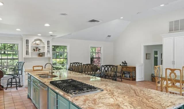 The kitchen of a Mendham, NJ house before renovation, with teal-painted cabinetry, a granite island and a vaulted ceiling over the breakfast room