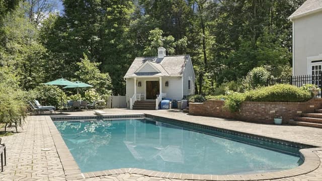 The pool at a Mendham, NJ property before renovation, a curved pool in a paver surround with the poolhouse on the bank behind it