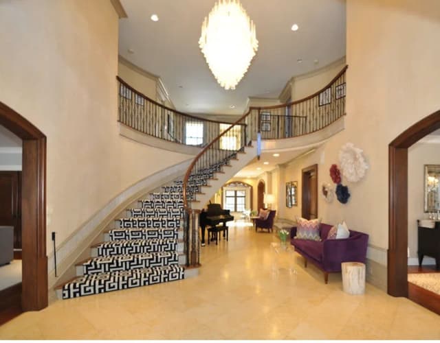 The double-height foyer of a Summit, NJ home before renovation, with a curved stair in a black and white geometric runner and a grand piano beyond