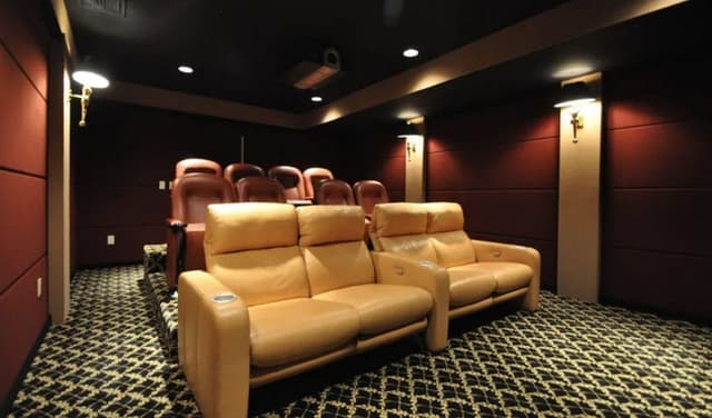 The lower-level theater of a Summit, NJ home before renovation, with tiered seating in tan leather against dark red walls