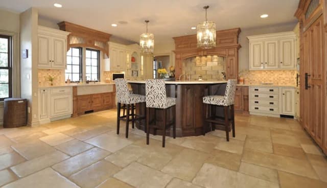 The kitchen of a Summit, NJ home before renovation, with cream raised-panel cabinetry, a travertine floor and a dark wood island