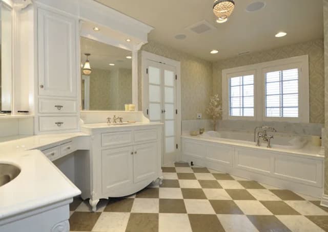 The primary bathroom of a Summit, NJ home before renovation, with a white vanity, a drop-in tub and a checkerboard tile floor