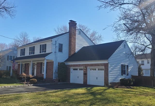 The front of a Westfield, NJ colonial before its exterior renovation, in white siding with a brick chimney and a two-bay garage wing