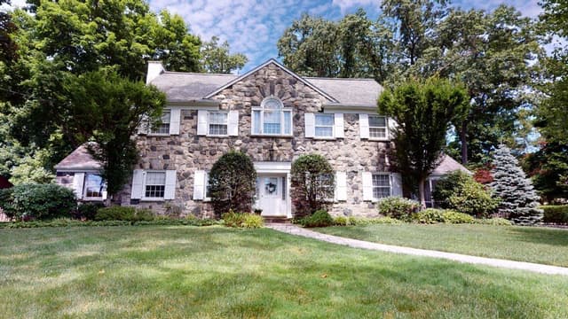 The front of a stone colonial in Westfield, NJ before renovation, with white shutters, overgrown foundation planting and a narrow concrete walk