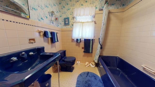 A bathroom in a Westfield, NJ home before renovation and addition, tiled floor to ceiling in blue with a matching tub and twin basins