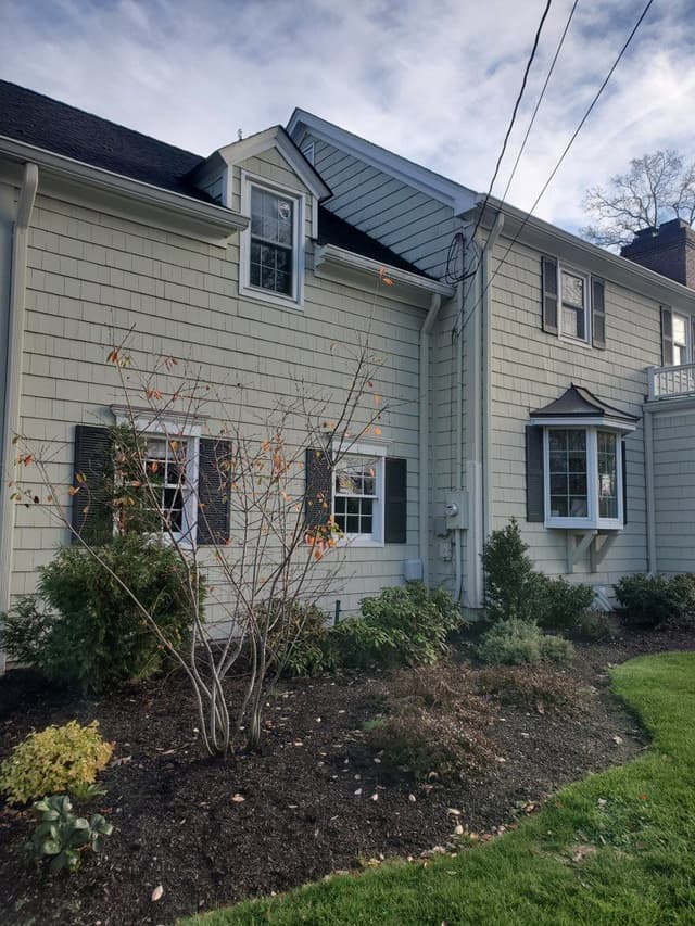 The side of a Westfield, NJ colonial before its exterior renovation, in plain white siding with a bay window and shrubs along the base