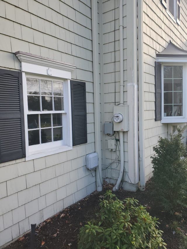 A close view of the siding and a window of a Westfield, NJ colonial before its exterior renovation, with the meter and the downspout on the wall