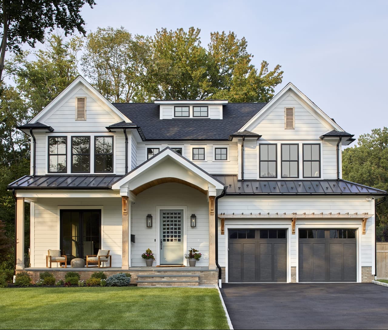 Front exterior of a white clapboard custom home in Westfield, NJ, with gabled dormers, a standing-seam porch roof and bronze garage doors, built by Michael Robert Construction