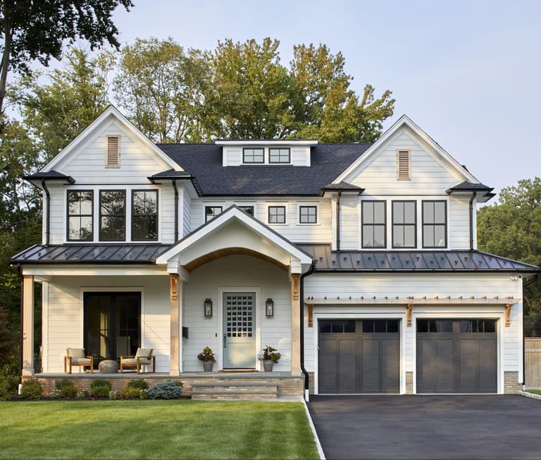 Front exterior of a white clapboard custom home in Westfield, NJ, with gabled dormers, a standing-seam porch roof and bronze garage doors, built by Michael Robert Construction