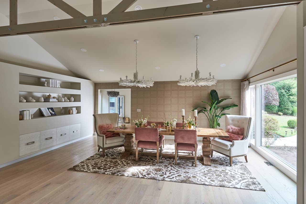 Dining room under a vaulted ceiling with exposed trusses, built-in shelving and two chandeliers