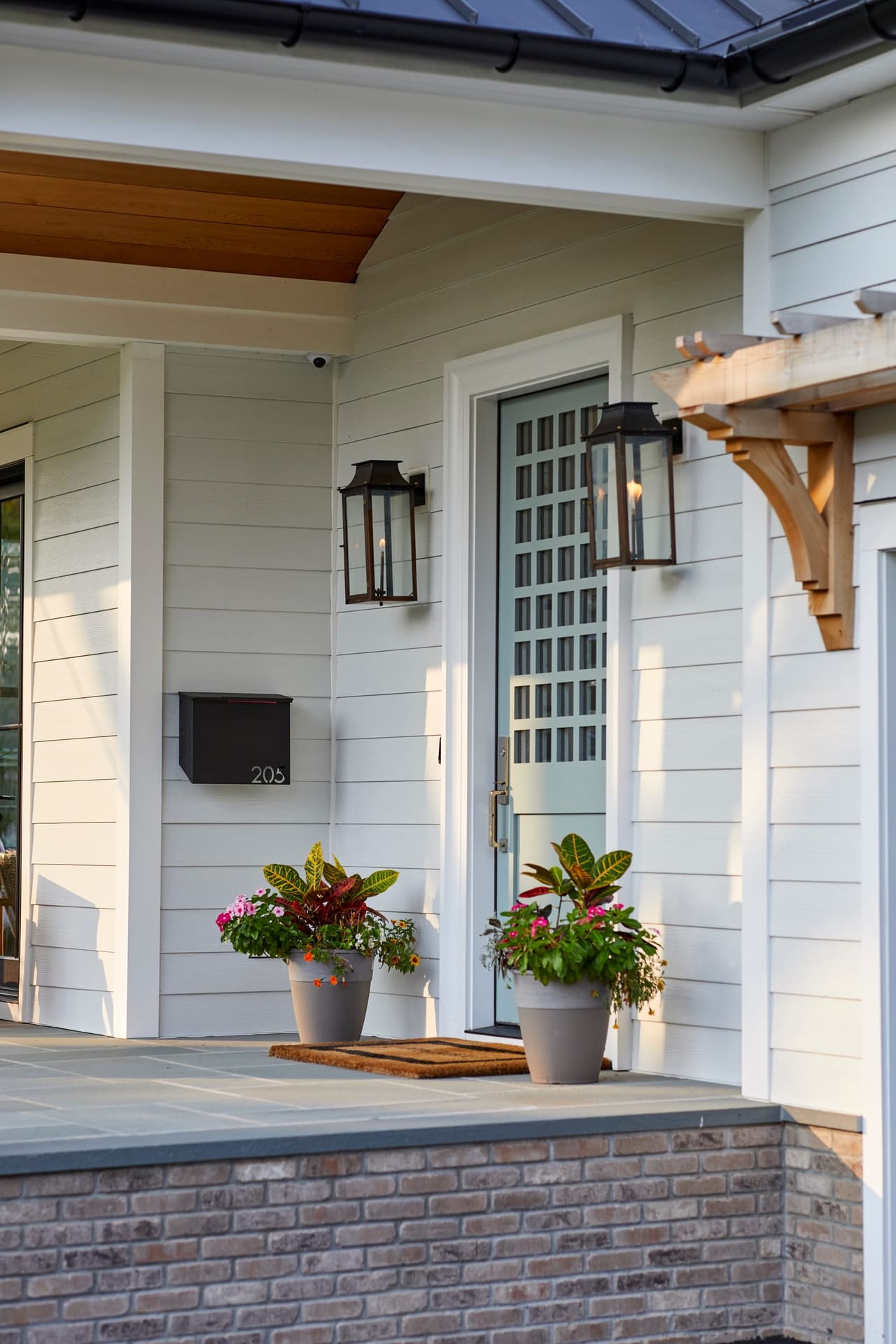 Front door of a Westfield, NJ new-construction home under a cedar-bracketed hood, with gas lanterns, planters and a brick step