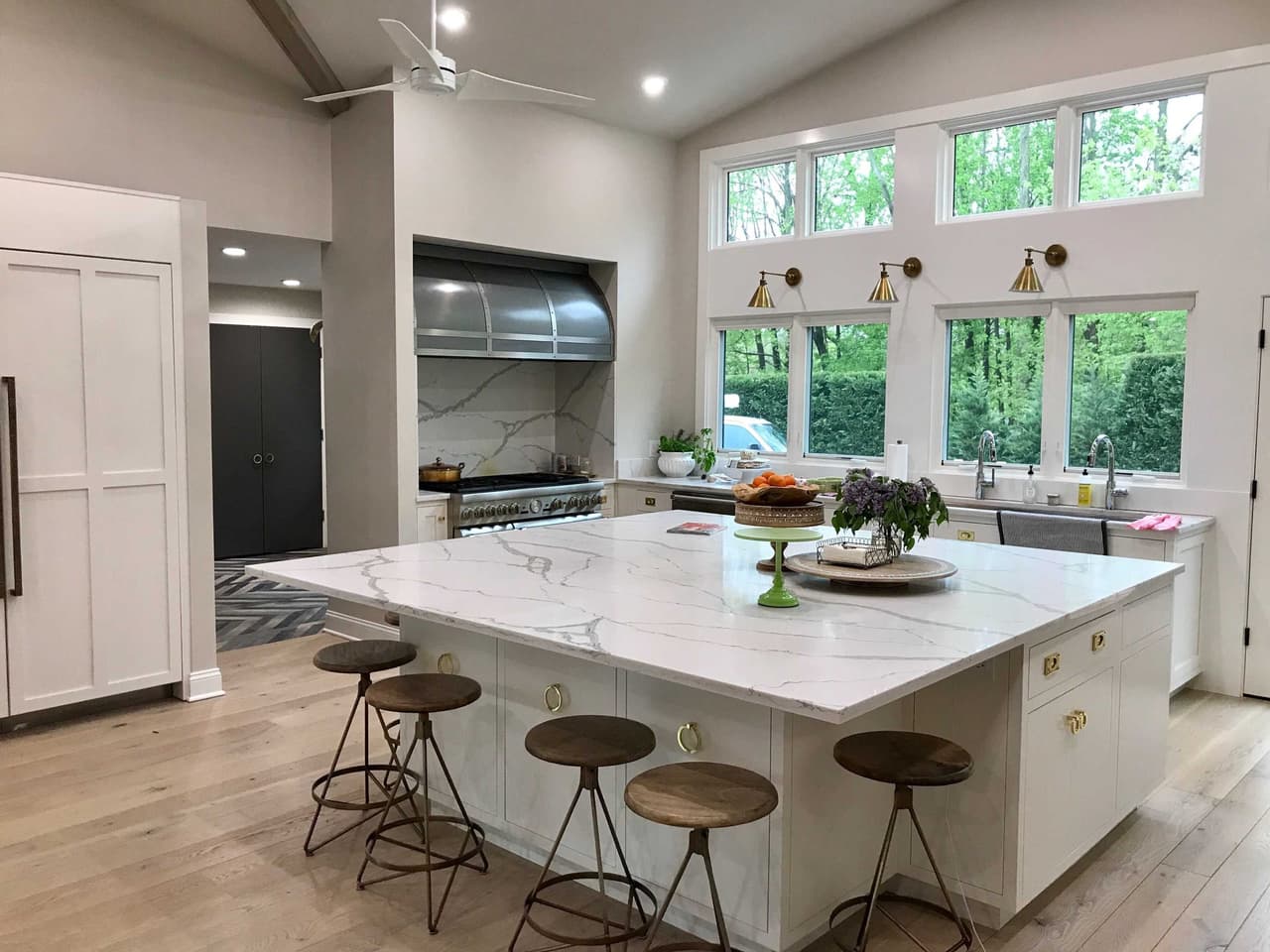 Marble island with five stools in a Scotch Plains, NJ farmhouse kitchen, under a vaulted ceiling with windows along the top of the wall