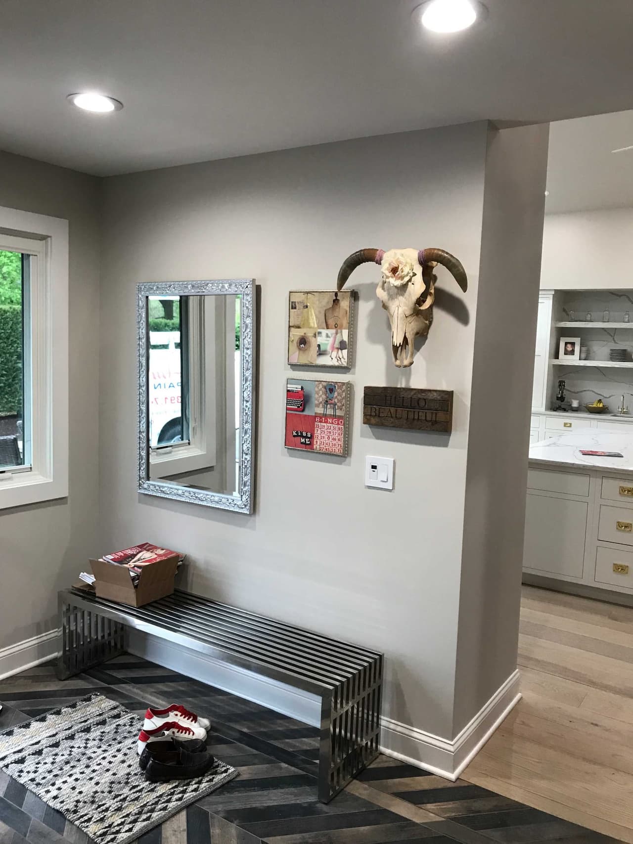 Entry with a silver-framed mirror, a mounted ram's skull and a metal bench on a patterned runner