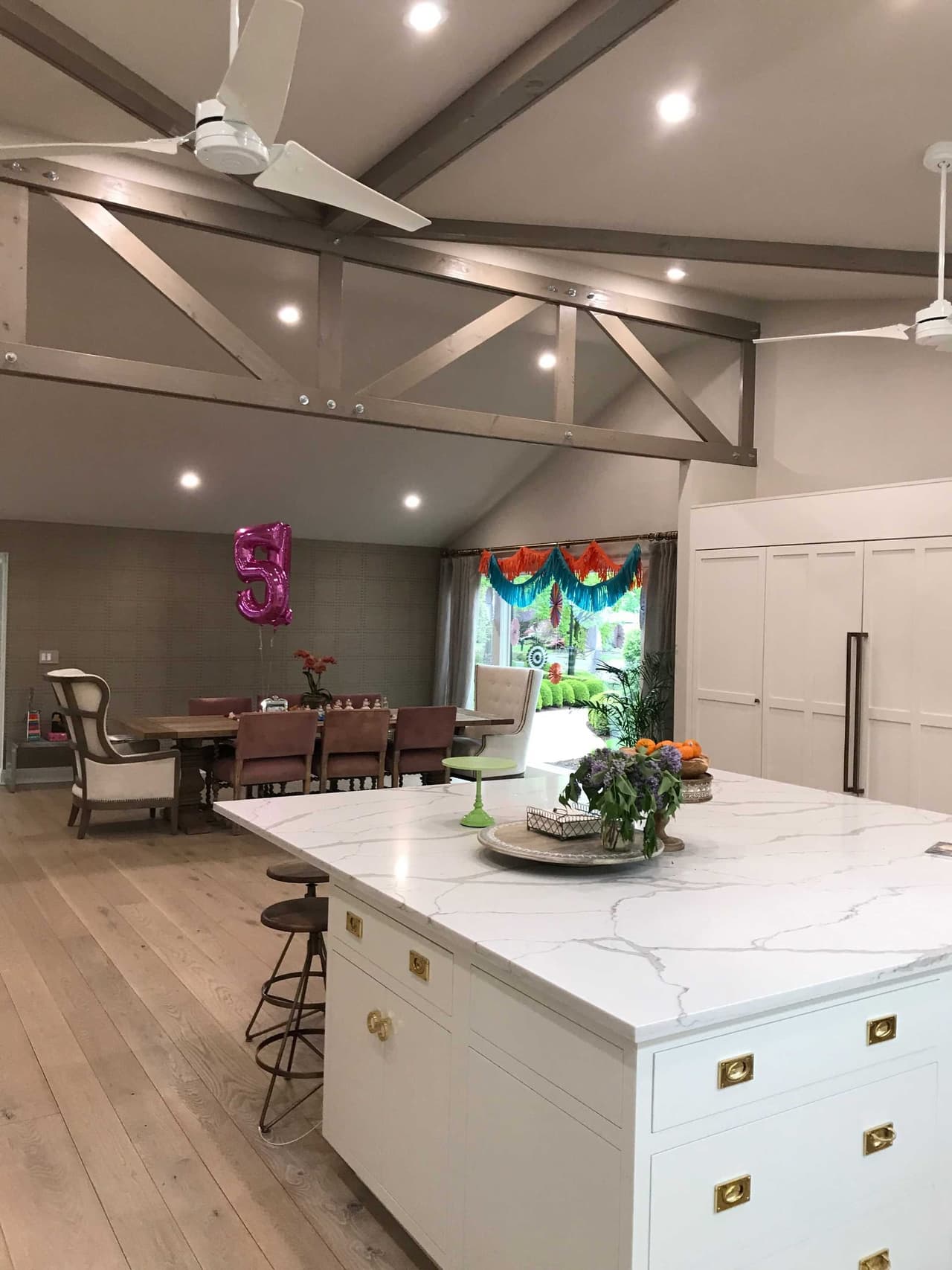 Kitchen island in marble beneath a vaulted ceiling with stained trusses and a ceiling fan, open to the dining area