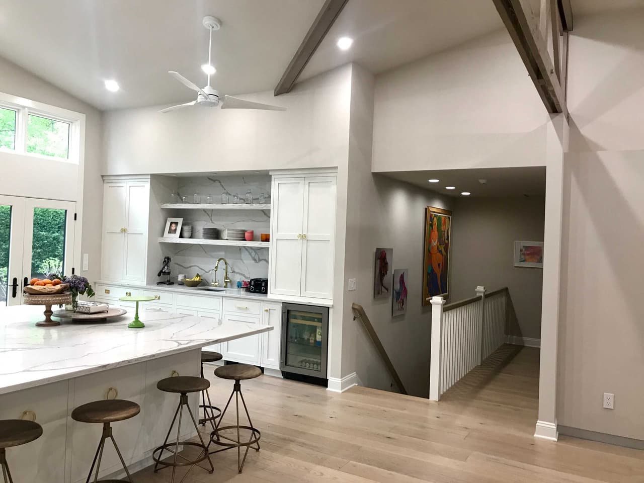 Kitchen under a vaulted ceiling with stained trusses, a marble island with counter stools and a view through to the stair
