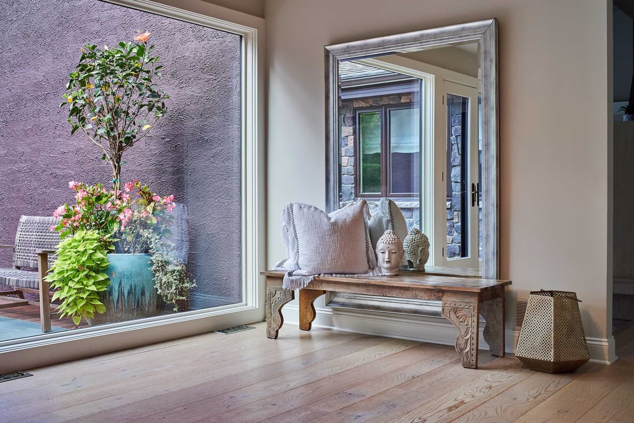 Bedroom corner with a large leaning mirror, a wooden bench and a picture window onto the garden