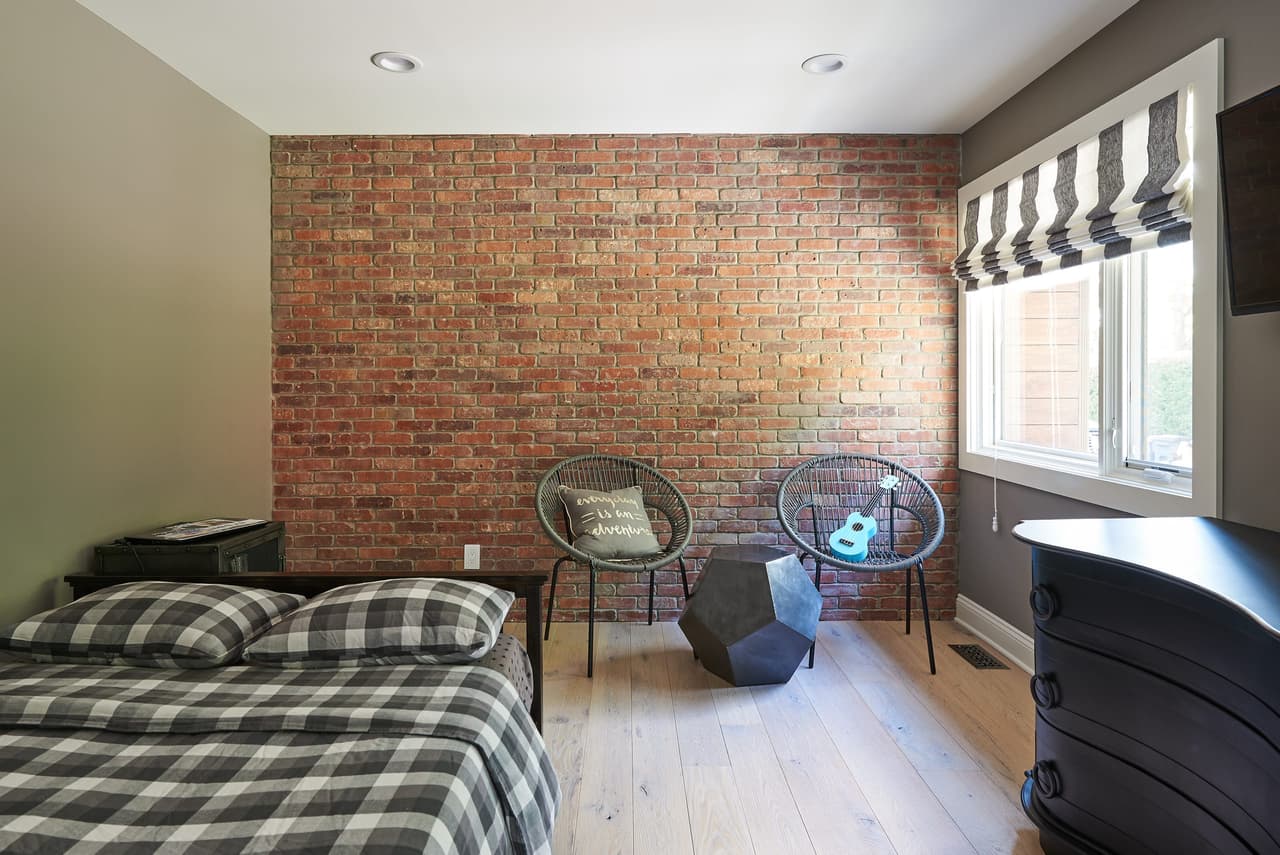 Bedroom with an exposed brick accent wall, a buffalo-check bed and two woven hoop chairs
