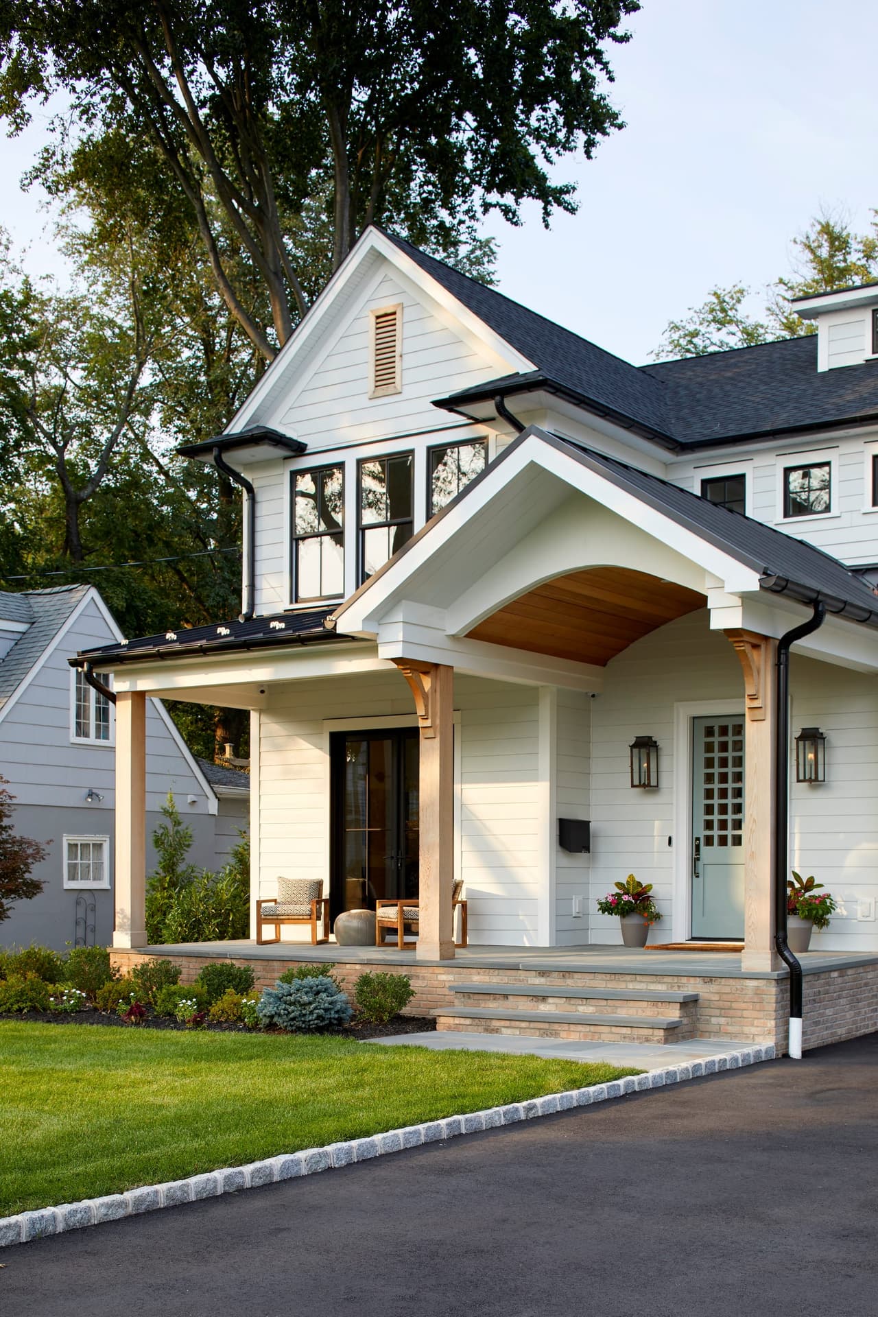 Front porch of a Westfield, NJ custom new-construction home, with a bracketed gabled portico, shingled gable ends and lanterns either side of the door
