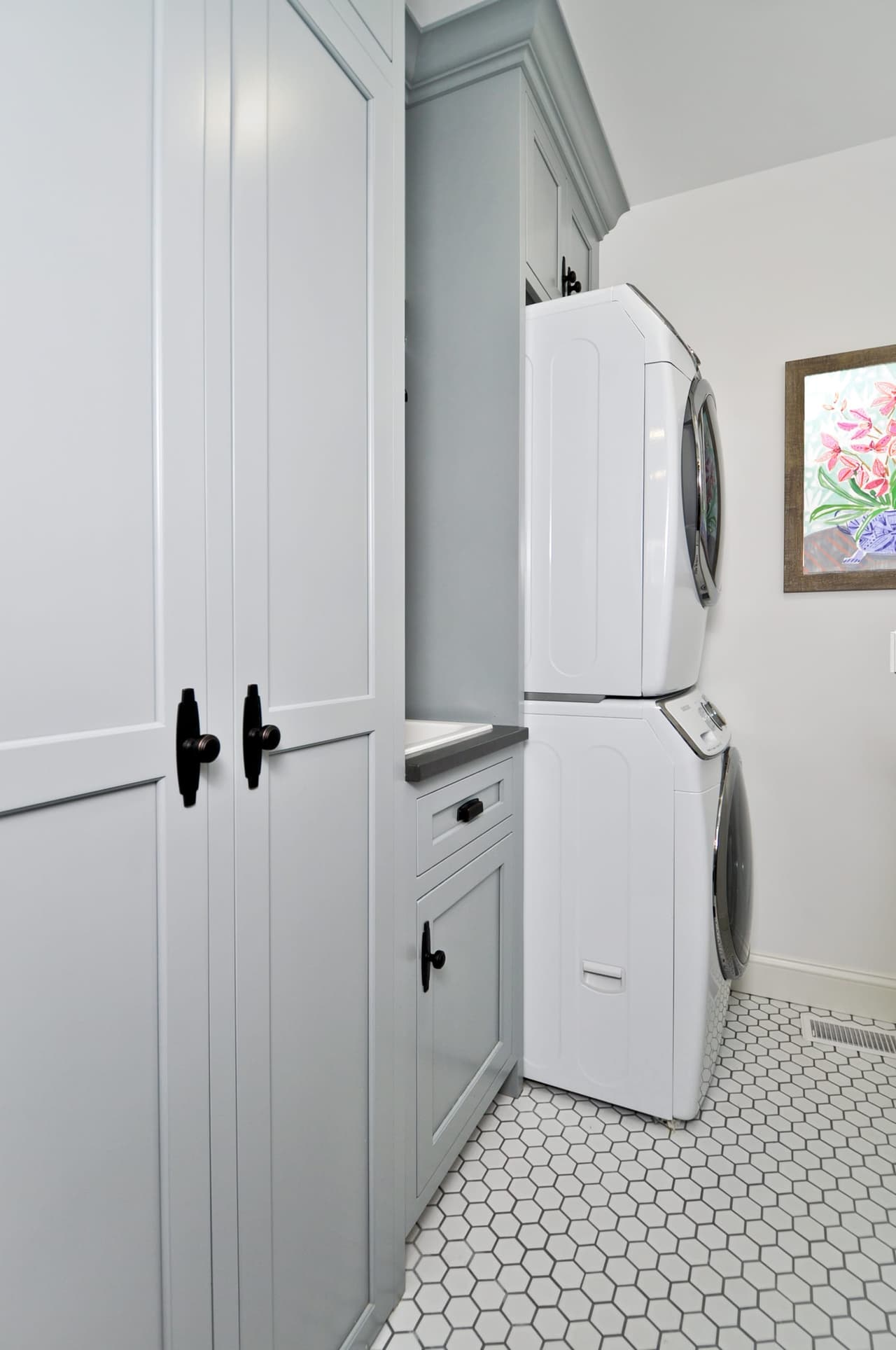 Laundry with a stacked washer and dryer in a built-in surround, pale cabinetry and a hexagon tile floor