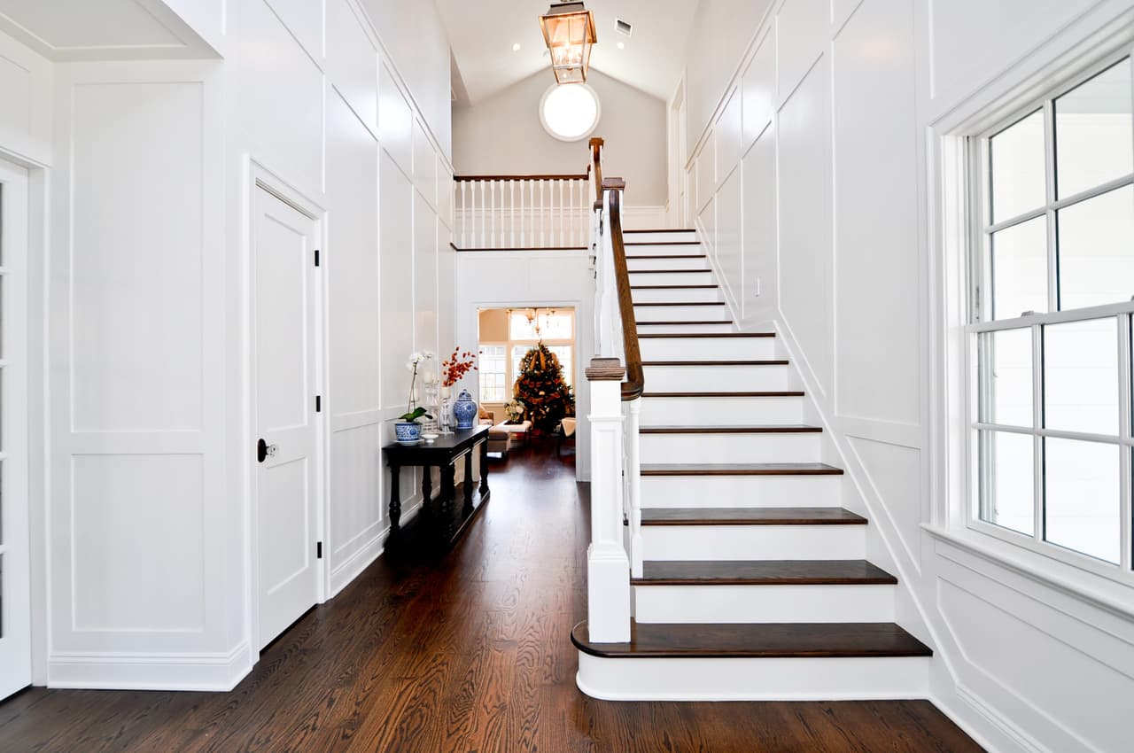 Entry hall with a white-painted stair, paneled walls and dark stained oak floors running the length of the house