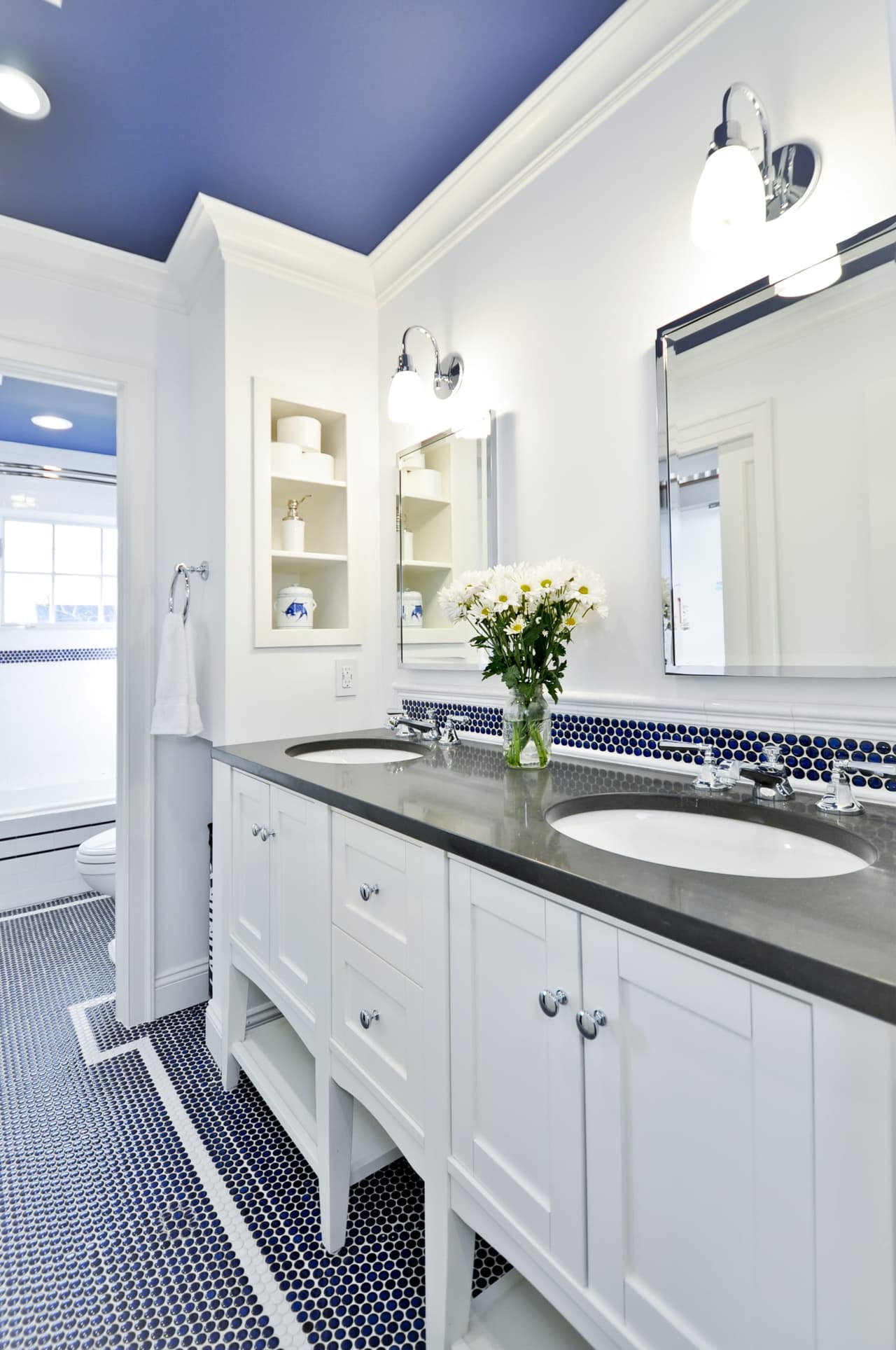 Bathroom with twin oval sinks in a dark counter, framed mirrors between sconces and a navy painted ceiling