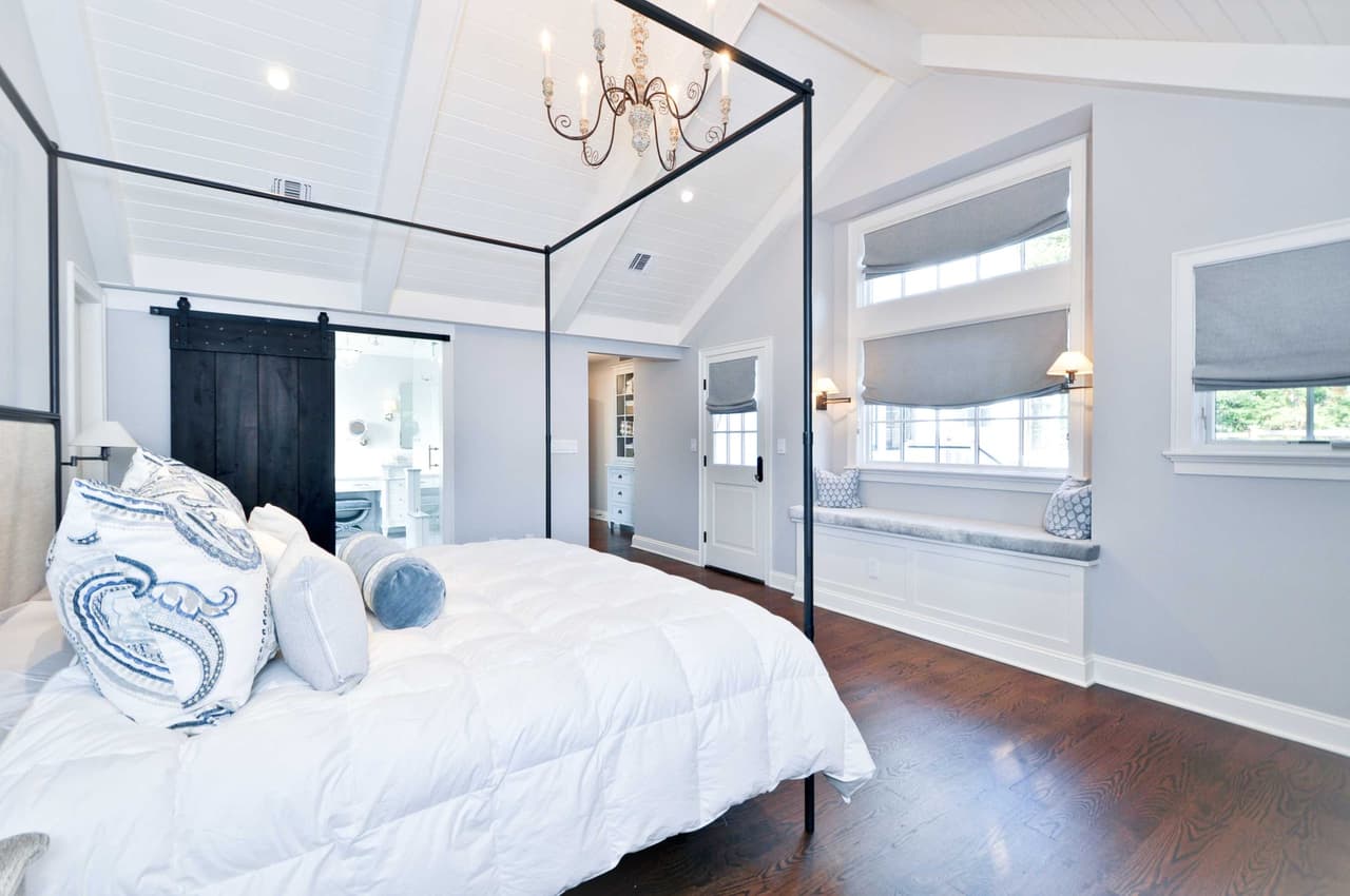Primary bedroom with a four-poster canopy bed, a dark barn door and a vaulted ceiling