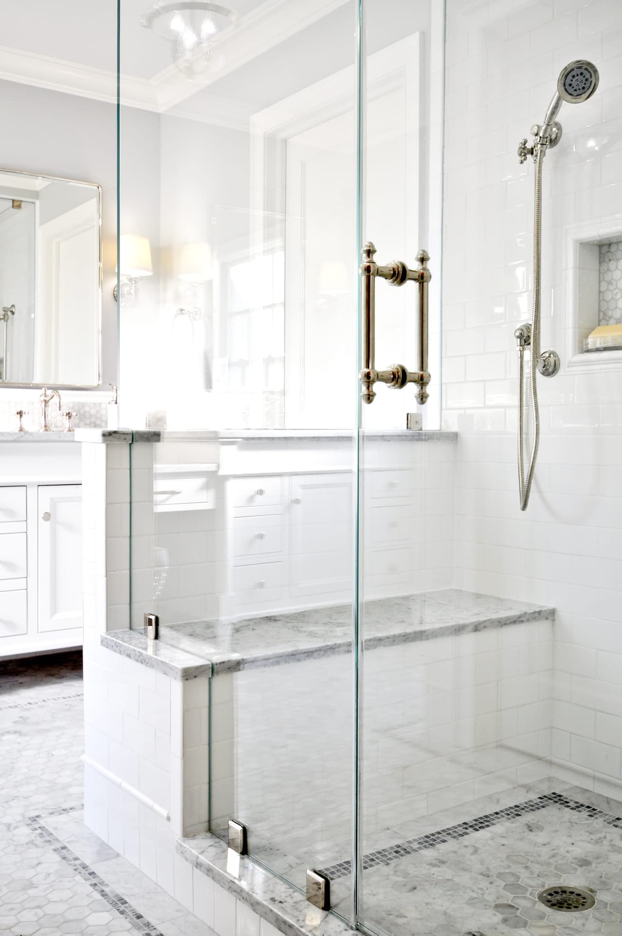 Glass shower enclosure with a marble curb, a built-in bench and a handheld and fixed shower head
