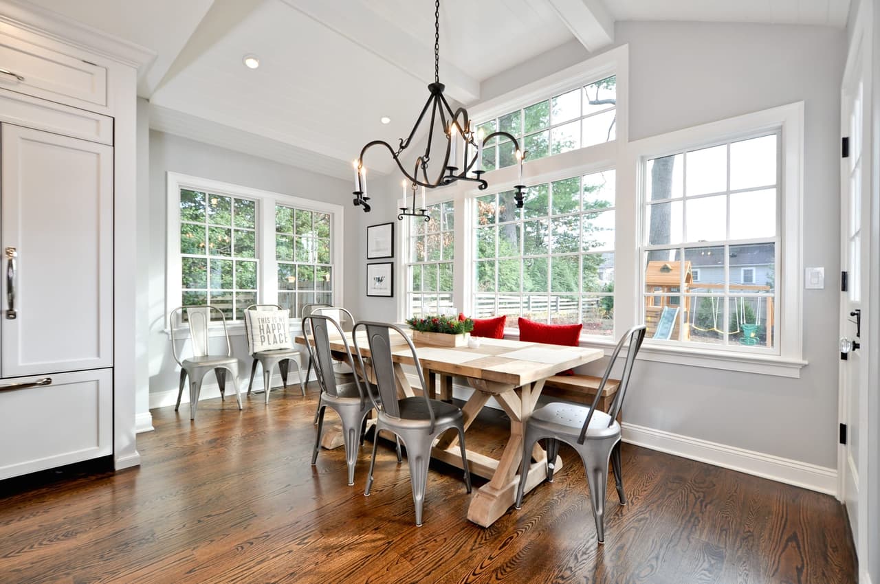 Breakfast room in a window bay with a trestle table, mixed seating and an iron chandelier