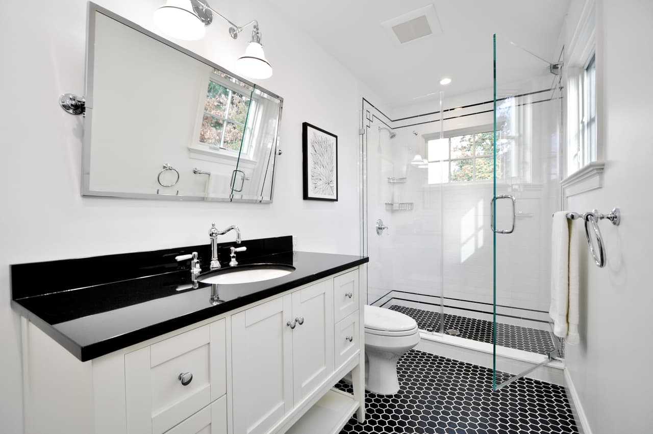 Bathroom with a black stone counter, a glass shower enclosure and a black-and-white penny tile floor