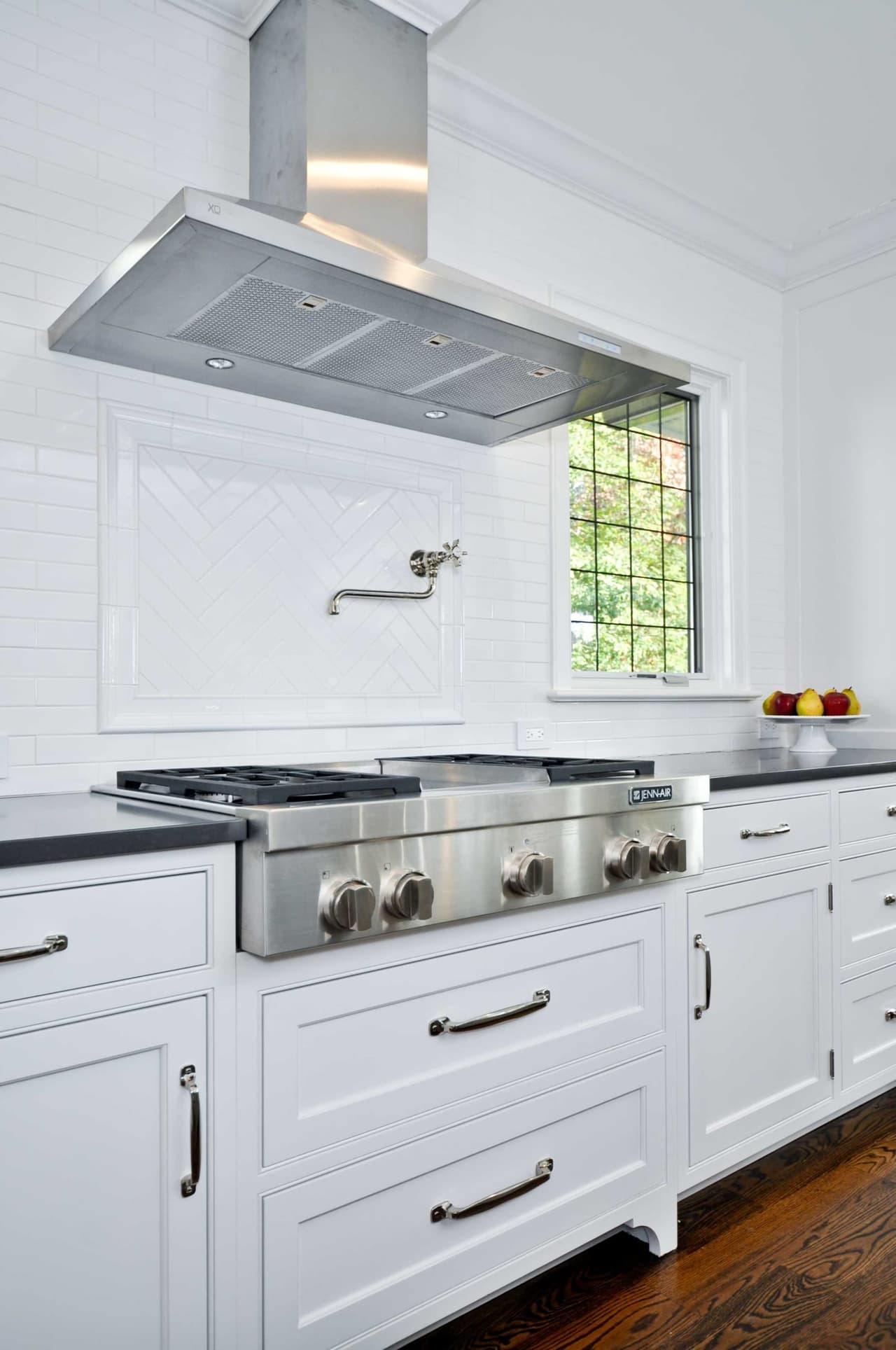 Range wall with a stainless hood, a professional range, a pot filler and white tile set against dark counters