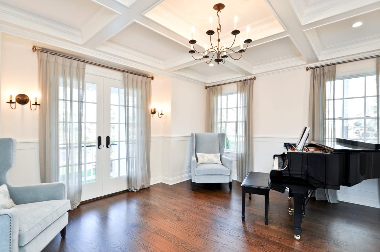 Living room with a coffered ceiling, French doors, wing chairs and a grand piano
