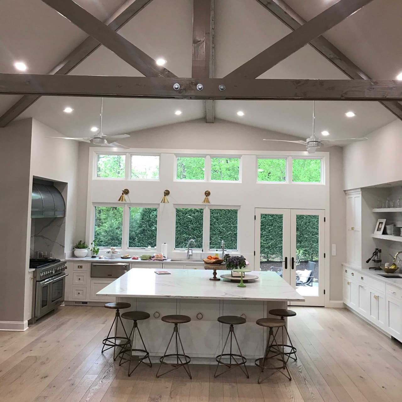 Kitchen of a Scotch Plains, NJ farmhouse renovation under an exposed truss, with a marble island, a clerestory of windows and French doors to the garden