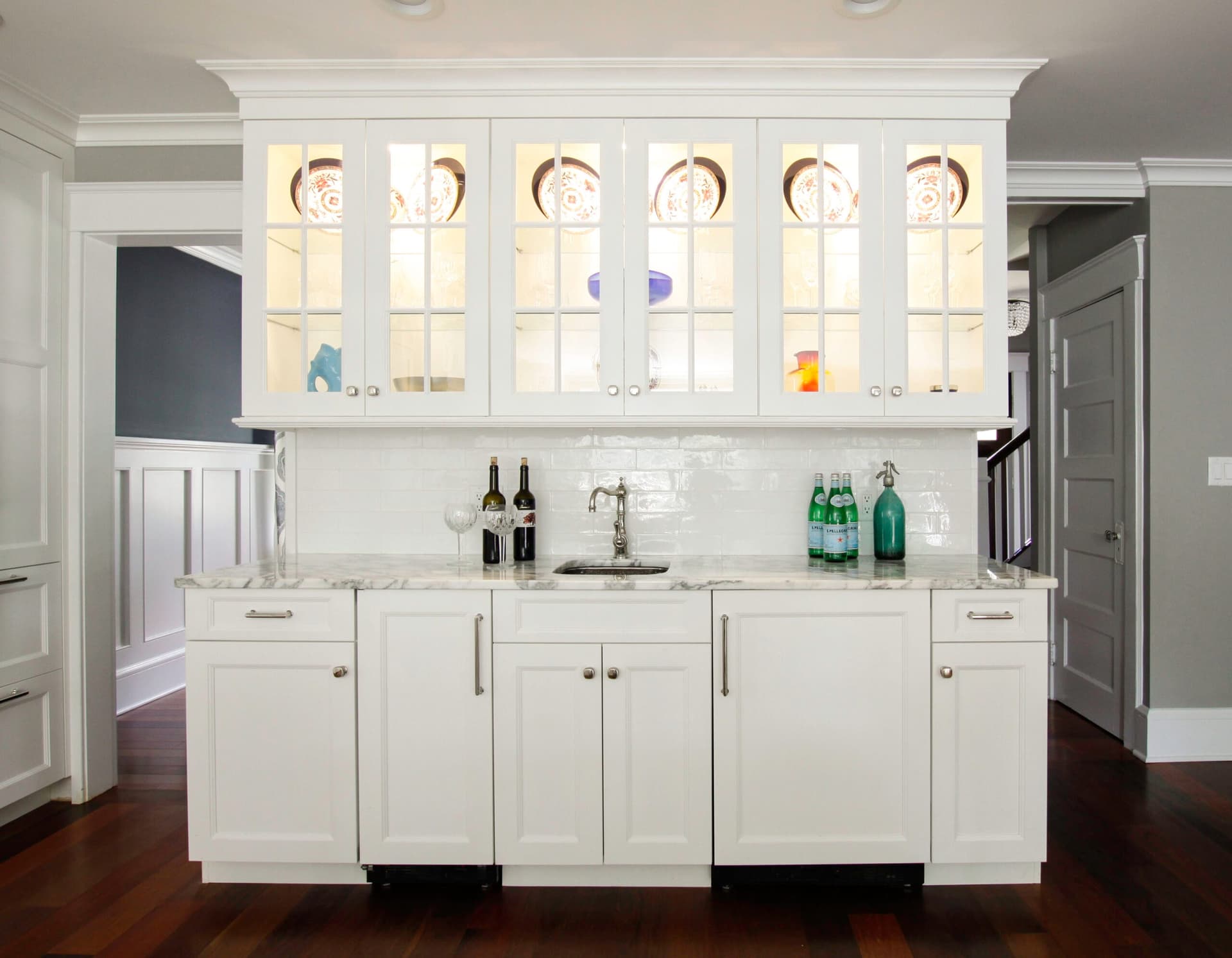 Butler's pantry with white inset cabinetry, lit glass-front uppers, a marble counter and subway tile backsplash