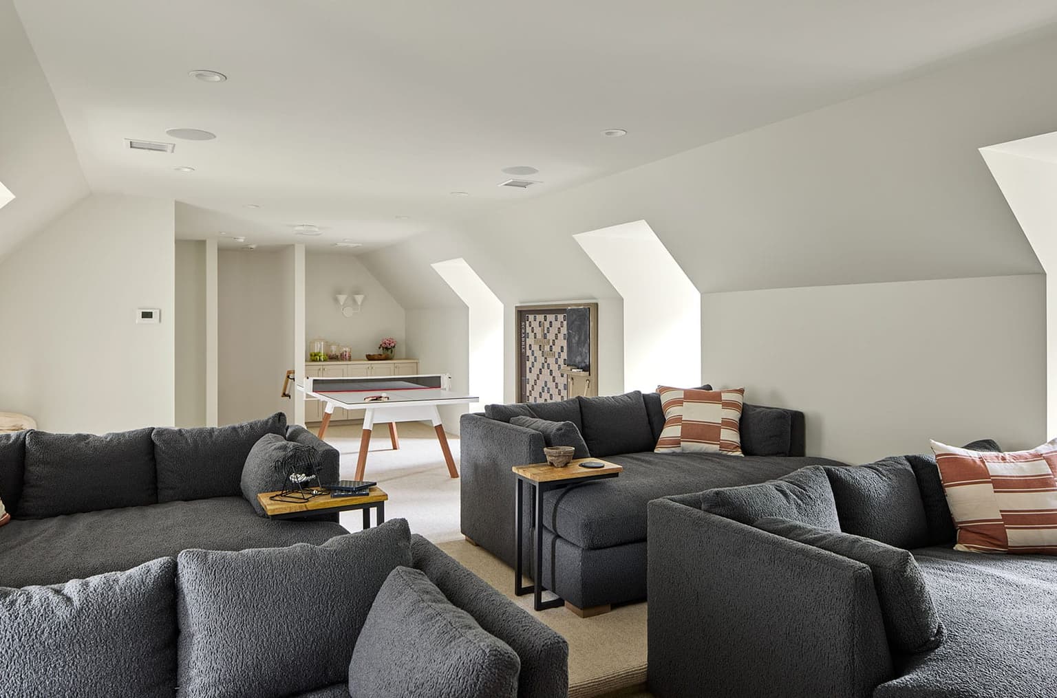 Home theater under a sloped ceiling, with two charcoal sectionals facing the screen and a games table behind them