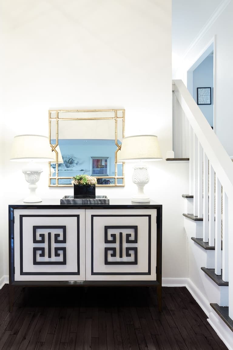 Entry with a black-and-white fretwork console between two lamps, beside a white-balustered stair