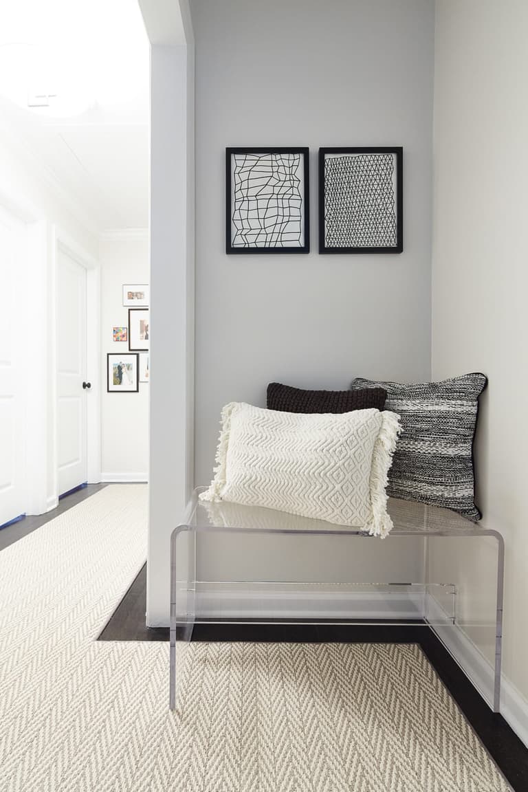 Upstairs hall with a lucite bench, two framed prints above it and a woven runner