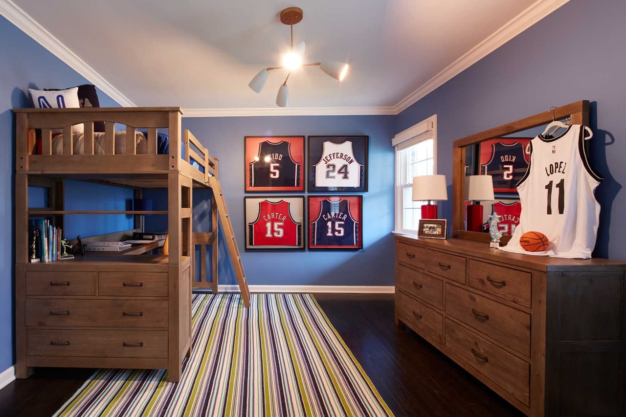Boys' bedroom with bunk beds, a navy accent wall of framed jerseys and a striped rug