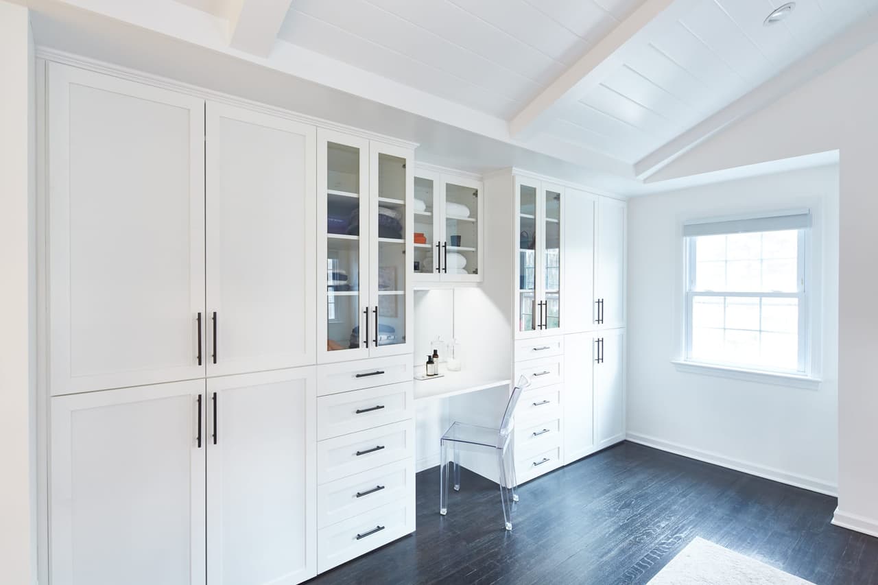 Dressing room in a Westfield, NJ renovation, with floor-to-ceiling white cabinetry down one wall, a built-in dressing table and a dark stained floor
