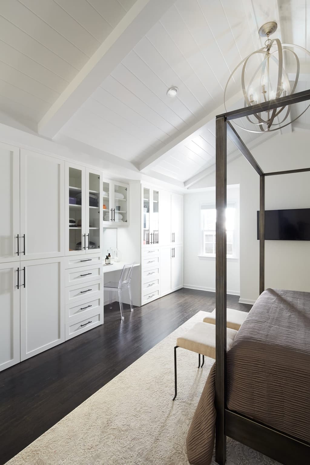 Bedroom under a vaulted ceiling with a black four-poster bed, an orb chandelier and a wall of white built-in cabinetry