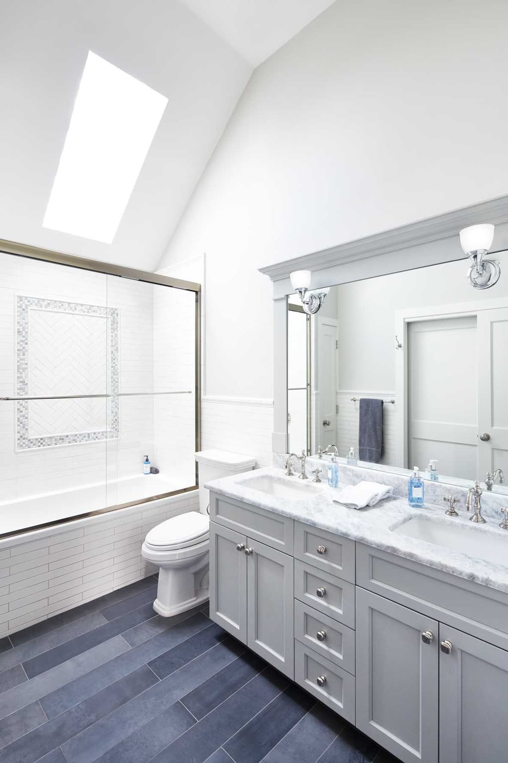 Bathroom in a Westfield, NJ renovation under a sloped ceiling with a skylight, with a gray vanity, a marble top and a tub behind the glass screen