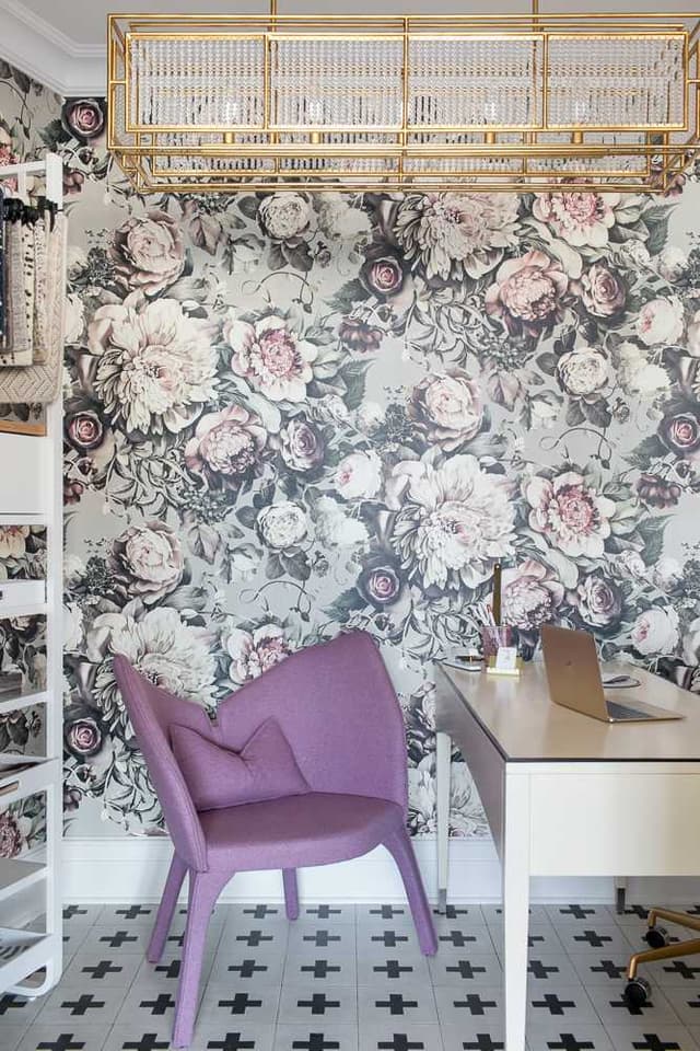 Desk against a large-scale floral wallcovering, with a lilac chair and a brass cage pendant above