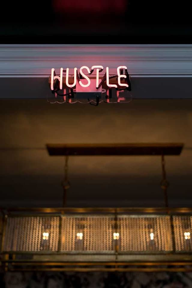 Neon sign reading HUSTLE above a long brass pendant in the MRC and Ellie Mroz Design studio in Westfield, NJ